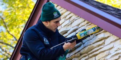 Worker sealing house wall with caulk gun.