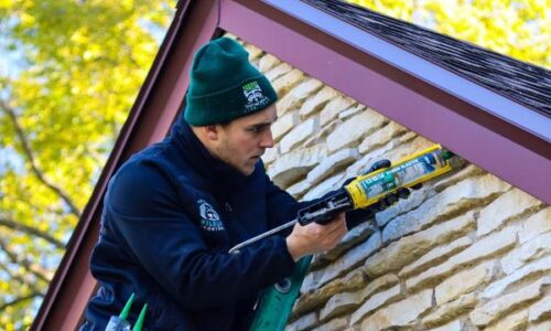 Worker sealing house wall with caulk gun.