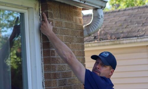 Man inspecting brick wall near window.