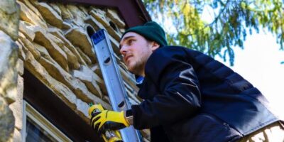 Man on ladder fixing house exterior wall.