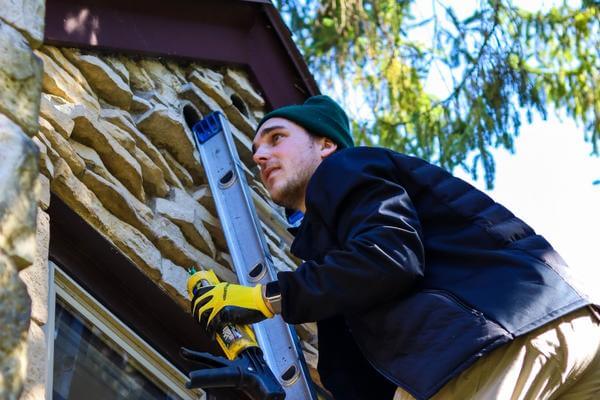 Man on ladder fixing house exterior wall.